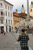 Man with fishing poles and string making bubbles for children in the Town Square of Ljubljana Slovenia with Robba Fountain and C