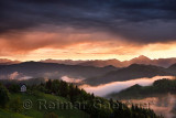 Pink sunrise and blue clouds in the mountains of Kamnik Savinja Alps with Storzic peak on right and fog over Skofjelosko Hills n