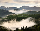 Rolling fog at sunrise with mountains of Kamnik Savinja Alps at Skofjelosko Hills with St Thomas church near Ljubljana Slovenia