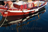 Man painting a classic wood sailboat moored at the marina in Izola Slovenia with reflection in the clear blue water