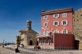 Red stucco apartment on the Adriatic Sea coast at Piran Slovenia next to the Punta lighthouse and 13th century Church of St Clem
