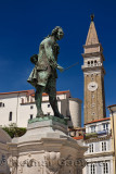 Close up of violinist Giuseppe Tartini statue in Tartini Square Piran Slovenia with St George's Parish church and bell clock tow