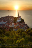 Setting sun on the Adriatic Sea with hillside trees below Town Wall of Piran Slovenia with City Hall, St Clement, St Francis, St