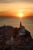 Setting sun on the Adriatic Sea behind Archangel Michael on top of belfry of St George's Cathedral of Piran Slovenia