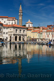 Piran Slovenia with inner harbor lined with boats and Tartini Square and St George's Cathedral and baptistery with belfry reflec