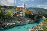 Colorful stucco houses on the turquoise Soca River with stone bridge at old section of Kanal Slovenia with Assumption of Mary ch