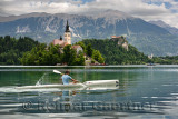 Assumption of Mary pilgrimage church Beld Island and kayaker on Lake Bled with Bled castle on cliff and Sol massive of Karavanke