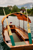 Traditional hand crafted wood Pletna boat with painted oars and canopy on Lake Bled with Bled castle and Vila Preseren Slovenia