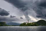 Cloud descending over Assumption of Mary belfry on Bled Island over Lake Bled at dawn with Bled Castle Slovenia