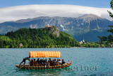 Traditional Pletna boat with colorful canopy on Lake Bled with Bled castle on cliff and St Martin church Sol massive of Karavank