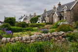 Flower gardens under cloudy sky with stone houses of Baile Mor village on Isle of Iona Scotland UK