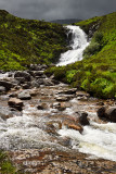 Sun on Blackhill or Eas a Bhradain waterfall on the Allt Coire nam Bruadaram river with dark clouds Scottish Highlands Isle of 