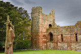 Life size statue of St Aidan first bishop of Lindisfarne facing ruins of the medieval priory on Holy Island of Lindisfarne Engla