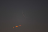 Jet contrail passing by a thin moon in the morning sky