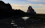 The sun casts darkness on the wall and colors Shiprock