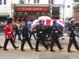 The bearer party walk alongside the coffin. The crowd applauds as a mark of respect.