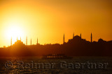 Sun setting over Blue Mosque with Hagia Sophia in silhouette on the Bosphorus with boat Istanbul