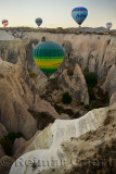 Hot air balloons over a steep canyon of eroded volcanic tuff and cave houses in Cappadocia Turkey