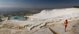 Panorama of woman in bikini on white travertine terraces at Pamukkale hot springs Turkey overlooking village and valley
