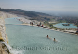 Mineral water flowing into hot spring pools depositing travertine terraces with tourists and bathers at Pamukkale Turkey