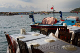 Restaurant tables at waters edge with fishing boats in harbor village of Assos Iskele Behram Turkey