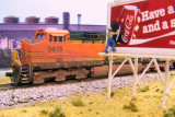 BNSF AC4400CW passes by man finishing installing Coke sign on the billboard