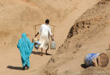 Man carrying buckets and a colorfully dressed woman disembarking at Old Dongola
