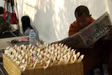 Monk reading newspaper beside his crafts
