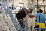 Assisting elderly man to climb railing for better position to watch procession