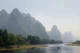 Tour boat rafts heading down the Li river Guangxi China with tall karst mountain cones in haze