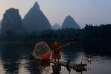 Fisherman with cormorant on pole on the Li river Yangshuo China with tall karst limestone peaks at dawn