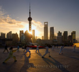 Sunrise shining through the Oriental Pearl Tower onto Tai Chi group exercising on the Bund Shanghai China