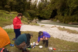 Janine, Roy, and Dave cooking tea alongside river campsite