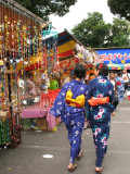 Yukata girls walking past a charm stall