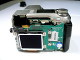The Top Cover is the first piece to put
back on to the camera. This can be a lesson
in frustration or at least make you wish you
had many hands.
The first thing that I did was to clean the
LCD Top Screen on the camera, then cleaned the
inside glass of the top cover. Handle with care
after this cleaning No Fingerprints Allowed.
Then it is time to re-attach the ribbon cable to its
connector keeping in mind the routing for the cable.
Then tilt/wiggle the cover and at this time open the Flash
Door and feed the Top Cover tab thru the opening, so
that the tab and screw align inside the flash compartment.
Handle with care, keep in mind that you do not want to break
the ribbon cable or disconnect it. Again keep your fingers
off the LCD and the glass. This is the hardest part of the
whole assembly, but take your time and you will get there.
