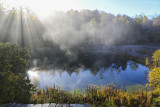 Rising sun through pond smoke on a frosty morning