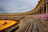 Groomers on the golden sand with empty stands at the oval Seville bullfighting ring