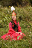 Young woman in traditional Kazakh dress sitting in a field at Huns village Kazakhstan