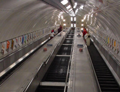 Another day begins...This photo was taken at the bottom of an escalator at a tube station.  I was looking up. It is cropped, so it is actually much longer. The colors you are seeing on both sides are small posters advertising plays, etc.  Sometimes the escalators break down, can you imagine going up the center stairway?  Remember, since this is cropped, there are a lot more stairs!