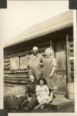 The Harris family on the front steps of the old log house on the farm east of Etomami. Standing: Ernest and Mamie  Sitting: Ken and Pearl.