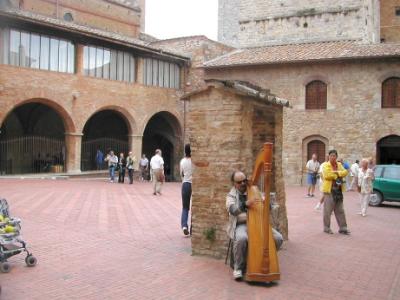 Harp player sits near a well (built in 1280's) on the Piazza Pecuri, next to the Piazza del Duomo