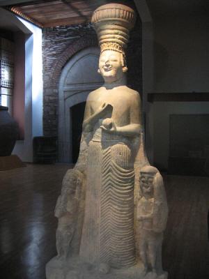 This figure was in a tall glass container and that's the reflection of the museum around her. 
 The tall head-dress ( polos ) and pleated dress indicate Greek influence.