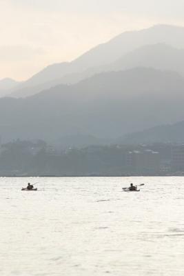 Kayakers going across the water towards the mountains of Hiroshima from Miyajima