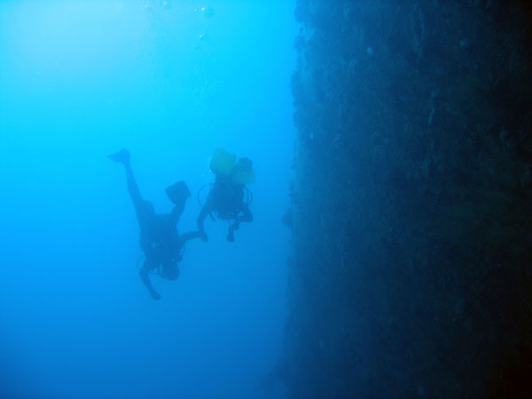 Two divers swimming along the huge hull of the Cedar Pride