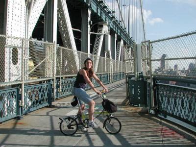 TU member Judy, astride her Brompton, smiles for the camera at the Manhattan tower of the Manhattan Bridge