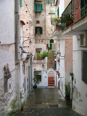 A passageway and houses. A satellite dish hangs on the white wall to the right - seems out of place here.