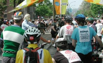 Trudy Hutter (in yellow), Steve Klein (in green & white wool jersey) and Hannah Borgeson (in blue) look on as one of the tour characters, dressed as a policeman (complete with badge and nightstick) inspects bicycles and keeps the crowd in line.