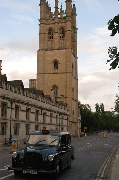 A taxi drives up High Street past the Bell Tower of Magdalen College