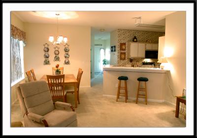 View from the sliders and the living room into the dining room, kitchen, and hallway toward the front of the condo. The den is on the left in the hall, opposite the guest room on the right.