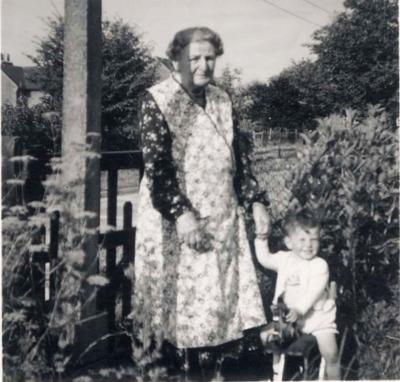 Nana and Andrew. She's has on one of the wrap-around pinnies she always used to wear.
Kim adds: Nana & me probably in front of Grannies place in Stoney Lane, Winchester (because we didnt move to Watton till I was a bit older & anyway there was no fences at the front in Watton; and Nanas place in Fair Oak had fields opposite). What is Nana holding in her right hand? Looks like the end of someones dick!!! Judging by the plants and trees its full summer so I guess Im 20-ish months old and its July/August 1949.